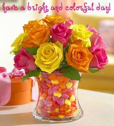 a vase filled with lots of colorful flowers on top of a table next to two cupcakes