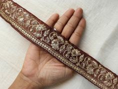 a hand holding a brown and gold colored ribbon with floral designs on the end,