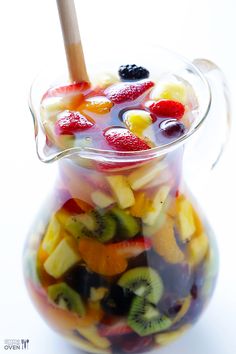 a glass pitcher filled with sliced fruit and a wooden stick in it's mouth