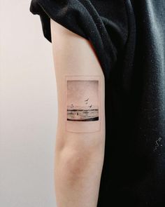 a person with a small tattoo on their arm that has birds flying over the water