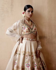 Editor's Note Presenting an opulent ivory raw silk lehenga set adorned with intricate floral thread embroidery and sumptuous velvet patchwork, elegantly highlighted with various embellishments. This captivating ensemble is paired with an embroidered blouse and dupatta, creating a regal and luxurious look perfect for grand occasions or elegant gatherings. The combination of the rich raw silk texture, the exquisite embroidery, and the ornate details on both the blouse and dupatta add a touch of op