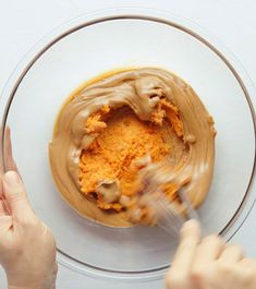 a person is spreading peanut butter on top of a cake in a glass bowl with two hands