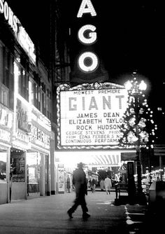 people are walking down the street in front of an old movie theater at night time