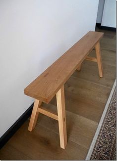 a wooden bench sitting on top of a hard wood floor next to a white wall