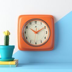 an orange square clock sitting on top of a blue shelf next to a potted cactus