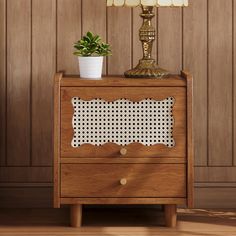 a nightstand with a lamp on top of it and a potted plant in the corner