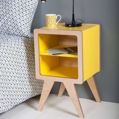 a yellow nightstand table with a laptop on it next to a pillow and bedding