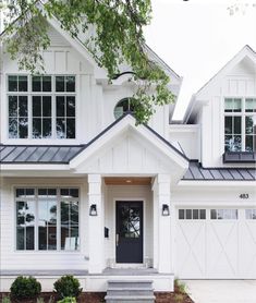 a large white house with black roof and two story windows on the front door is surrounded by greenery