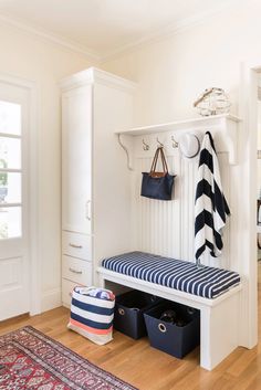 a white bench with blue and white stripes on it in front of a closet filled with purses