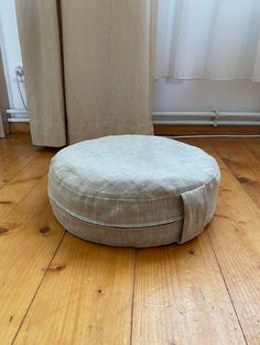 a round dog bed sitting on top of a hard wood floor next to a window