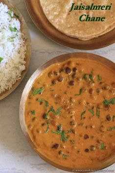 two bowls filled with food next to rice and pita bread on a white table