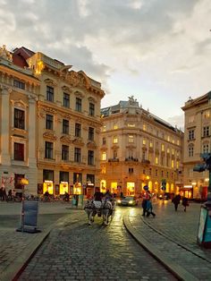 a cobblestone street with horse drawn carriages in the middle and people walking around