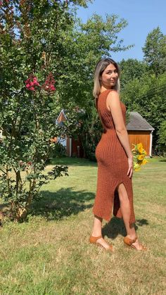 a woman is standing in the grass wearing a brown dress and tan slip - ons