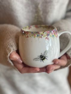 a person holding a coffee cup with a bee painted on it