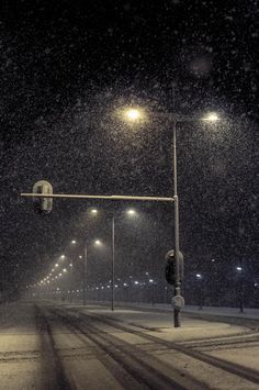 a street light on a snowy night with snow falling all over the ground and lights in the background