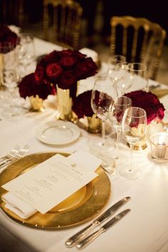 the table is set with white and gold plates, silverware, and red roses