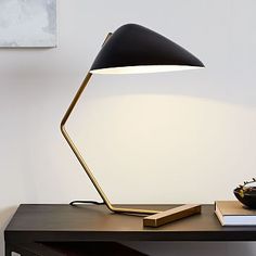 a desk lamp sitting on top of a wooden table next to a book and bowl