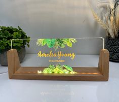 an acrylic sign that says, america young the owner on it with plants in the background