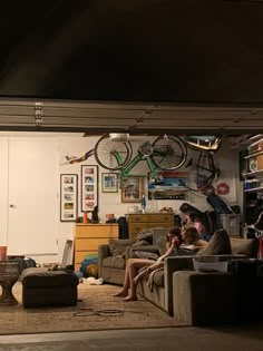 two people sitting on couches in a living room with bikes hanging from the ceiling