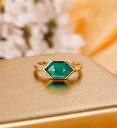 an emerald colored ring sitting on top of a gold box with flowers in the background