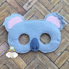 a blue felt mask with pink ears and eyes on a wooden floor next to a sticker