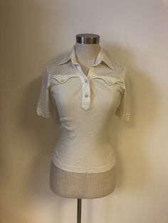 Awesome vintage tee from the 70s by Enea Gabrielli.  Off white with two pretend chest pockets. Semi sheer soft fabric at top part and sleeves and a ribbed fabric from chest pockets down at front and at back.  Great condition! But top button is missing and a little thread has come off the seam on the sleeve edge trim. 100% cotton Marked size 42 but estimated size S/M Please check measurements. Measurements taken laying flat; (Stretchy fabric) Shoulders 14,5" Bust 16,5" Waist 13 3/4" Length "21" Sleeves 8" Feel free to contact me with any questions! Retro Cream Cotton Tops, Retro Cream Cotton Top, Cream Cotton Retro Top, Vintage Cream Short Sleeve T-shirt, Fitted Collared T-shirt With Pockets, Fitted Retro Cream Top, Vintage Cream Cotton Top, Vintage Short Sleeve Cream T-shirt, Vintage Cream Short-sleeved T-shirt