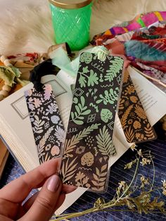 a person holding an open bookmark in front of some flowers and books on a table