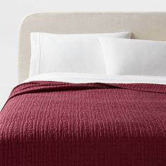 a bed with white pillows and red bedspread on top of the headboard