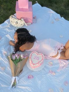 a woman laying on top of a blanket next to a cake and bouquet of flowers