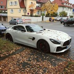 a white sports car parked on the side of a road next to a pile of leaves