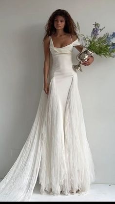 a woman in a white dress holding a flower and a silver vase with flowers on it