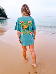 "Introducing the stunning Laguna Beach California tee! Perfect for all those who love the tropical vibes and laid-back beach lifestyle. Featuring a gorgeous coconut girl aesthetic, this shirt is adorned with an array of beautiful hibiscus, plumeria, and other tropical plants, creating a lush and vibrant design that's sure to turn heads. At the center of the design, you'll find an illustration of someone surfing at sunset, capturing the essence of the iconic California surf culture. The warm colo Blue Beach T-shirt With Front Print, Beachy Hawaiian Shirt With Tropical Print, Vacation Hawaiian Shirt With Tropical Print And Relaxed Fit, Hawaiian Shirt With Hibiscus Print For Beach Season, Relaxed Fit Tropical Print Hawaiian Shirt For Vacation, Relaxed Fit Hawaiian Shirt With Tropical Print For Vacation, Relaxed Fit Beachy Hawaiian Shirt For Vacation, Hawaiian Beach Tops With Hibiscus Print, Hawaiian Hibiscus Print Beach Tops