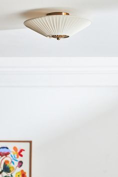 a white ceiling light hanging from the ceiling in a room with paintings on the wall