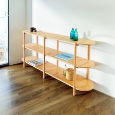 a wooden shelf with books on it next to a glass vase and bookcase in front of a window