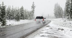 a white van driving down a snow covered road next to evergreen trees in the distance