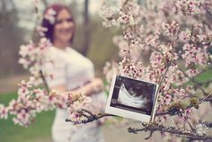 a woman standing next to a tree with pink flowers in the foreground and an image of a baby's stomach on it