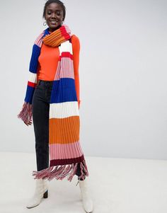 a woman wearing an orange, blue, and pink striped scarf standing in front of a white background