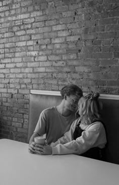 a man and woman sitting next to each other at a table in front of a brick wall