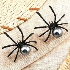 pair of black spider earrings with silver balls on them sitting on a piece of fabric