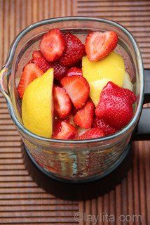 fresh fruit is in a blender on a mat with strawberries and lemons