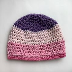 a crocheted beanie with pink, purple and white stripes sits on a table