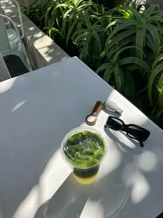 a bowl of green liquid sitting on top of a white table next to some glasses