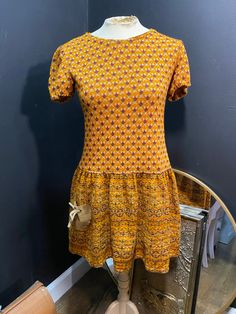 This dress is so cute!  From the 1960's, it was made by the brand Marjee Originals. It was also Union Made, meaning it was made by American garment workers back in the day! It is closest to a size small, possibly a medium, but here are the exact measurements taken lying flat and doubled: Shoulders: 15 inches  Chest: 30 inches  Waist: 30 inches  Hips: 33 inches  Shoulders to Hem: 31 inches   This dress is a beautiful orange knit with a smaller green, blue and red abstract pattern on it. It has a drop waist, puffed Juliet sleeves and a zipper going up the back. One small, leather pocket on the front is shaped like a heart and has ties on it. *There is one small mark on this pocket.*  This dress would look unbelievably cute with tights, boots and a cardigan this fall for a cozy look! Orange Knit Dress, Orange Knit, Garment Workers, Red Abstract, Leather Pocket, 1970s Fashion, Knoxville Tn, Union Made, Drop Waist