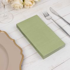 a place setting with flowers and silverware on a white wooden tablecloth covered in green napkins