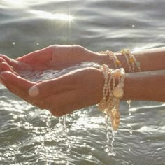 two hands holding something in the water with sunlight shining on them and beads hanging from their wrists