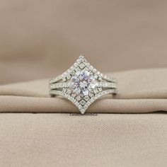 a diamond ring sitting on top of a cloth covered cushioned surface with the center stone surrounded by smaller diamonds