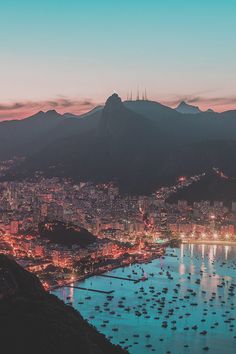 an aerial view of a city at night with boats on the water and mountains in the background