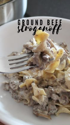 a white plate topped with pasta and meat covered in gravy next to a fork