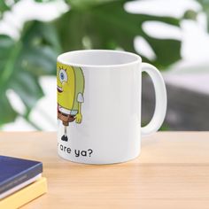 a white coffee mug with the words are you? on it next to a book