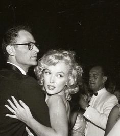 an old black and white photo of a man hugging a woman in front of other people